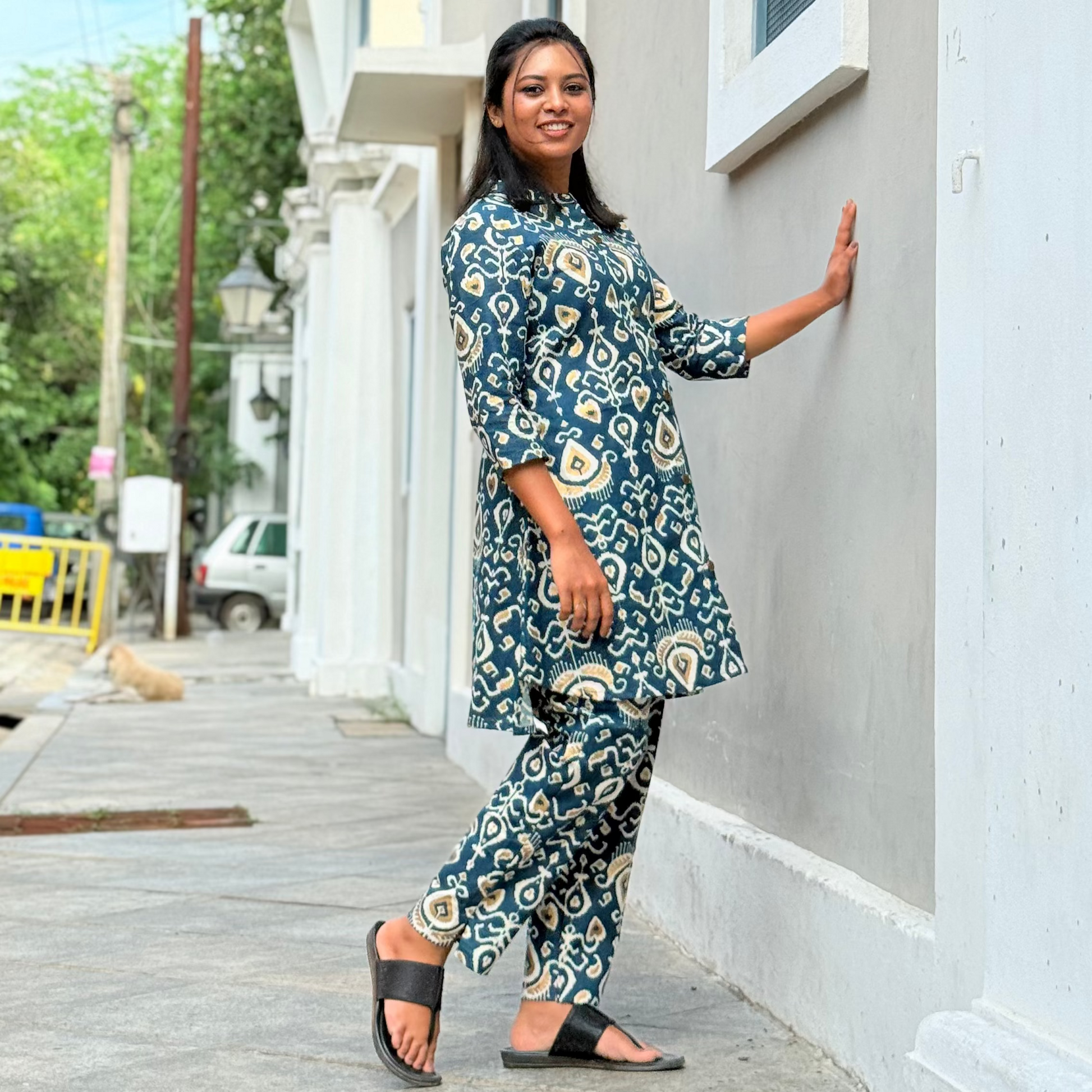 Woman in a blue floral outfit standing on a sidewalk next to a building.
