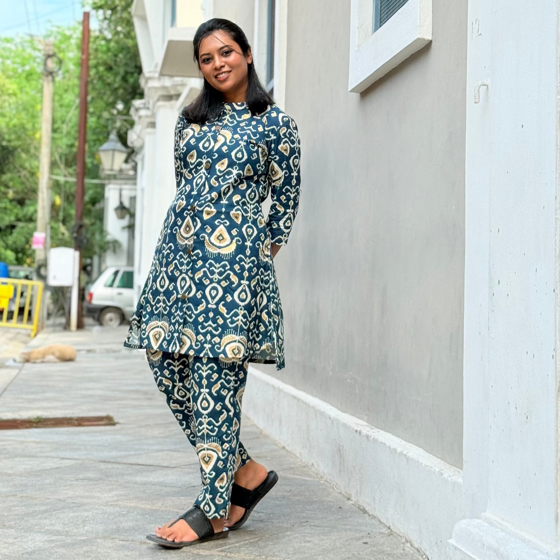 Woman wearing a blue patterned outfit standing on a sidewalk.